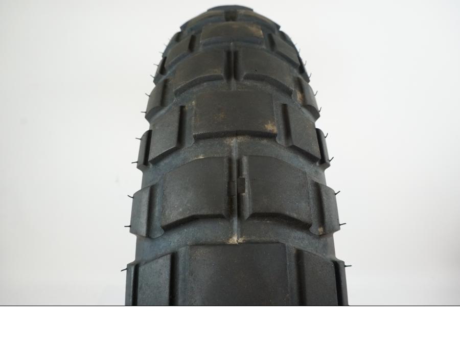 Baksidan på <p>Däck: Shinko Adventure Trail E-804.</p>
<p>Dimension: 120/70-R19 M/C 60 H.</p>
<p>Tillv. 0118</p>
<p>Mönsterdjup: ca. 40 %.</p> motorcykel.