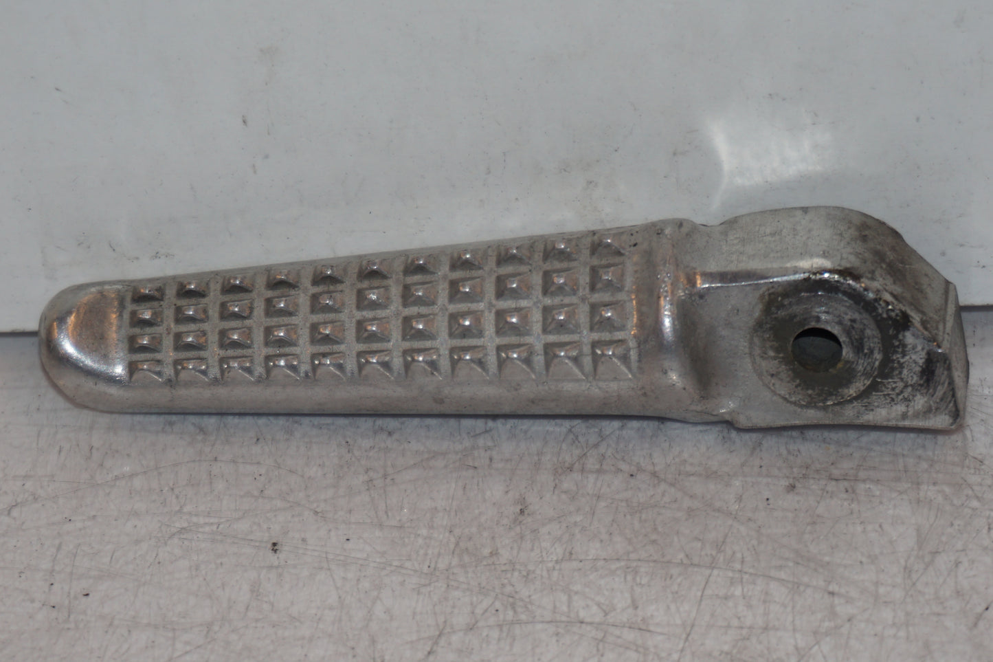 Framsidan på <p>Fotpinne höger bak från Honda VFR 750 F 1995.</p>

<p>Små märken på undersidan. Okej skick.</p> motorcykel.