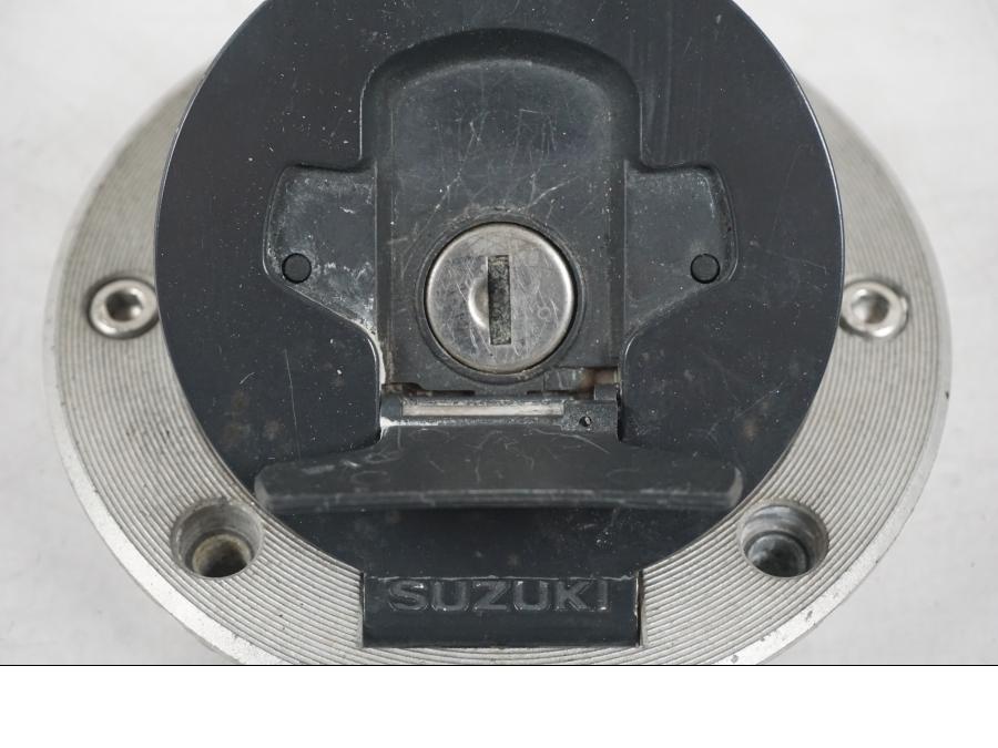 Snett uppifrån på <p>Låssats från Suzuki TL 1000 S 1997.</p>

<p>Tändningslås, tanklock, sadellås och 1st nyckel.</p>

<p>Repor finns på tanklocket, slitage av lack på tändningslåset även att gummi skyddet för kabel har ett hål se bild.</p> motorcykel.