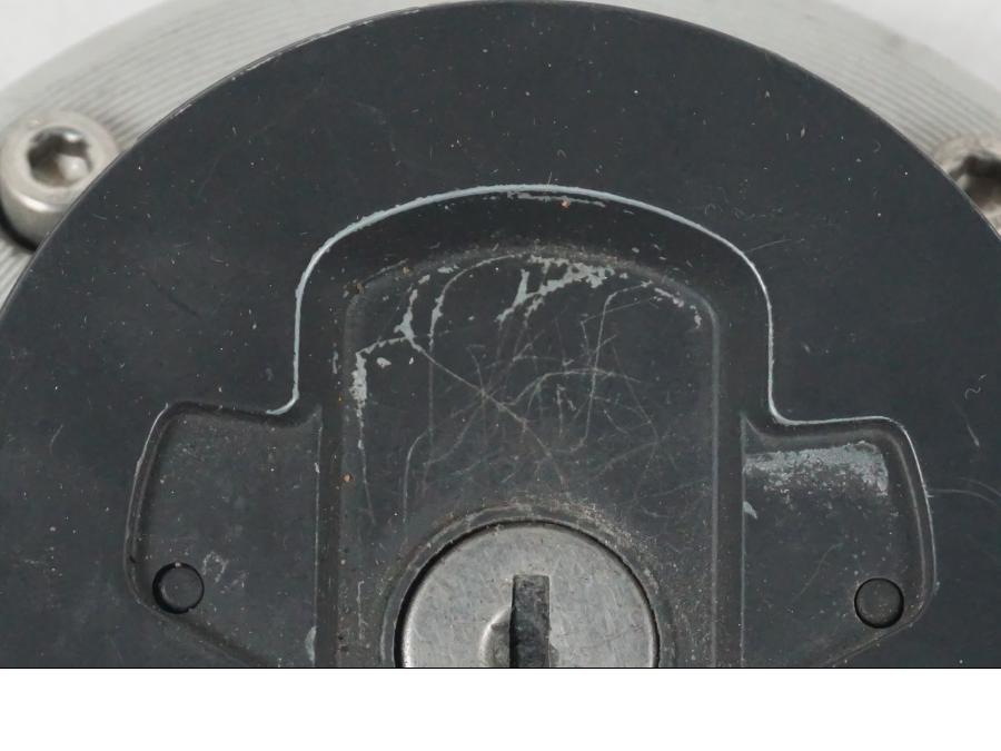 Snett nerifrån på <p>Tanklock från Suzuki GSX 750 W 2002.</p>

<p>Med 1st nyckel. Repor finns på tanklocket se bilder.</p> motorcykel.