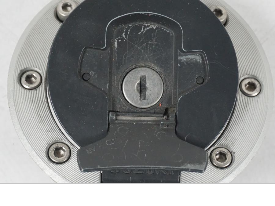 Snett uppifrån på <p>Tanklock från Suzuki GSX 750 W 2002.</p>

<p>Med 1st nyckel. Repor finns på tanklocket se bilder.</p> motorcykel.