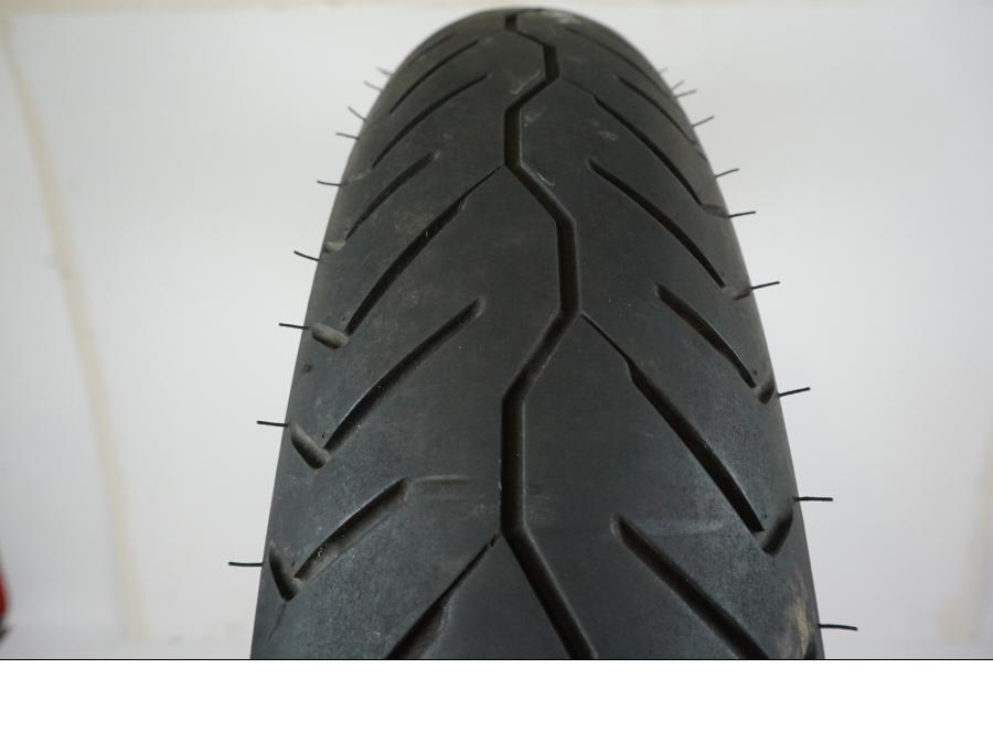 Baksidan på <p>Däck: Bridgestone Exedra Max F.</p>

<p>Dimension: 110/90-19 M/C 62H.</p>

<p>Tillv. 2814.</p>

<p>Mönsterdjup: ca. 40 %, lätt plattslitet och torrsprucket.</p> motorcykel.
